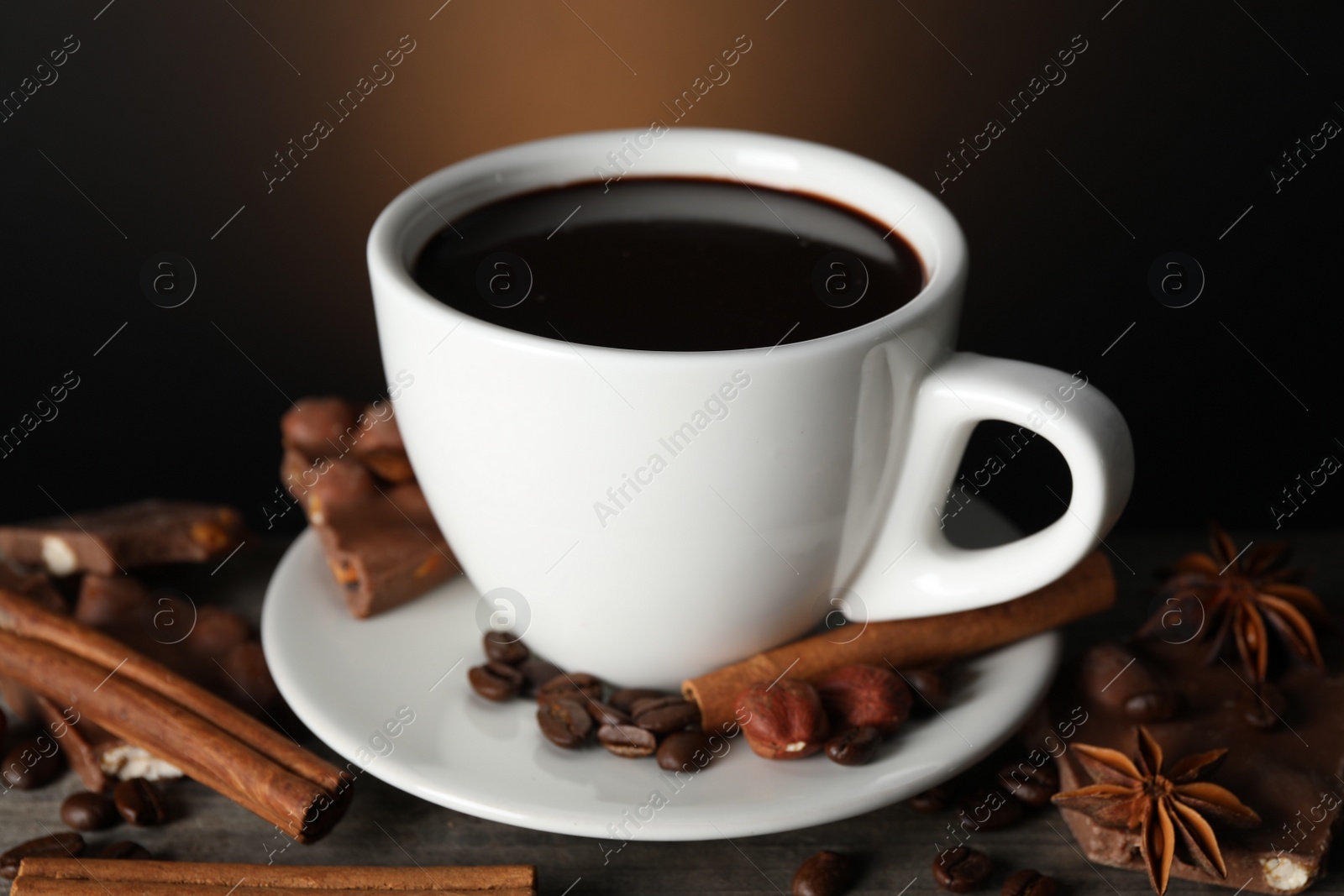 Photo of Cup of delicious hot chocolate, spices and coffee beans on wooden table