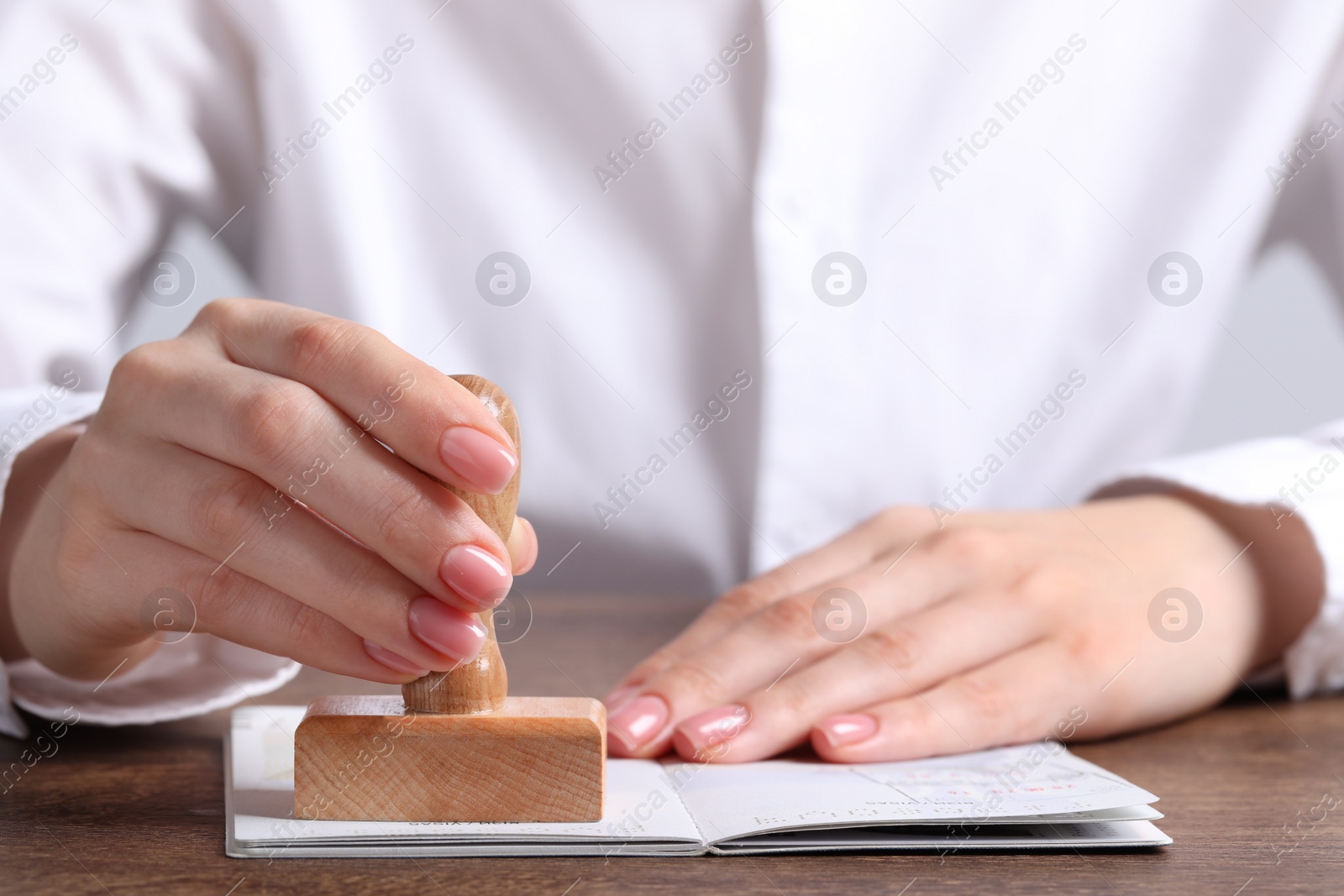 Photo of Ukraine, Lviv - September 6, 2022: Woman stamping visa page in passport at wooden table, closeup