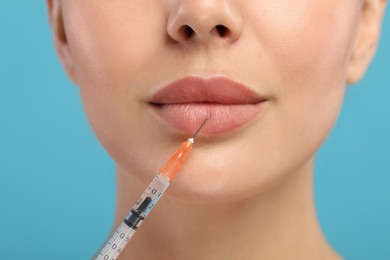 Young woman getting facial injection on light blue background, closeup. Cosmetic surgery