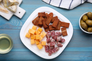 Photo of Toothpick appetizers. Pieces of sausage, cheese and croutons on light blue wooden table, flat lay