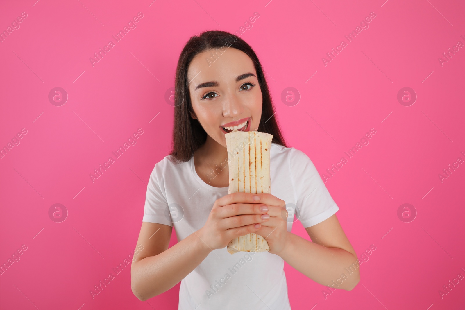 Photo of Young woman eating tasty shawarma on pink background
