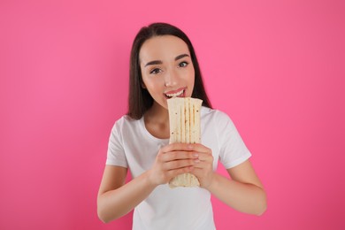 Young woman eating tasty shawarma on pink background