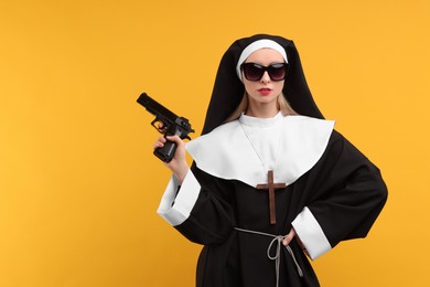 Photo of Woman in nun habit and sunglasses holding handgun against orange background, space for text