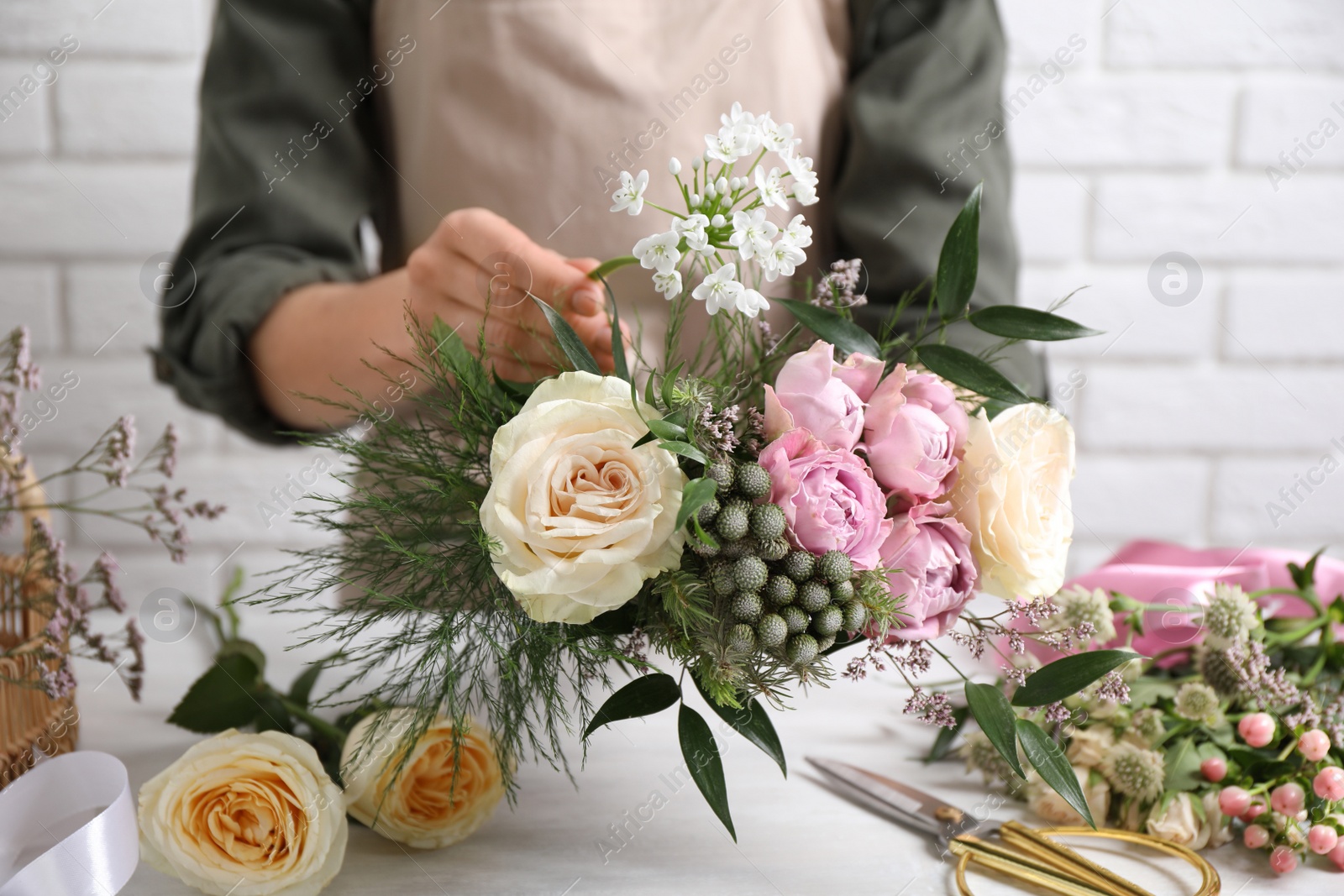 Photo of Florist making beautiful bouquet at white table, closeup