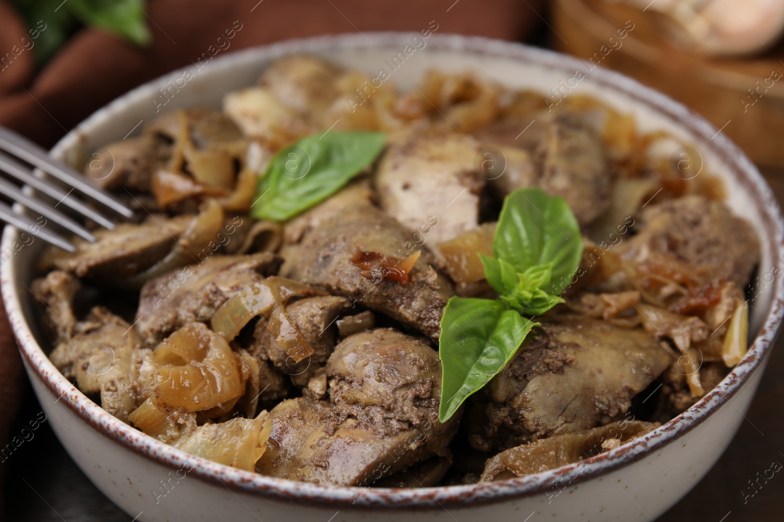 Photo of Delicious fried chicken liver with onion and basil in bowl on table, closeup
