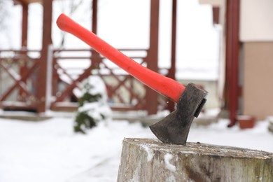 Photo of Metal axe in wooden stump outdoors on winter day