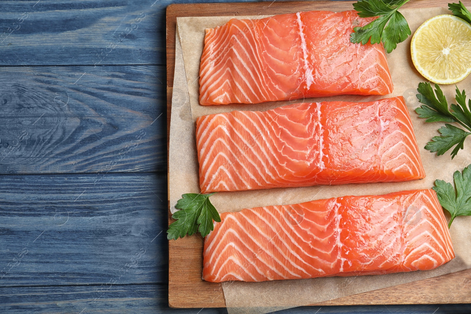 Photo of Top view of fresh raw salmon with parsley on blue wooden table. Fish delicacy