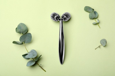 Metal face roller and eucalyptus on green background, flat lay