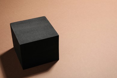 Photo of Black cube on light brown background, closeup and space for text. Stylish presentation for product