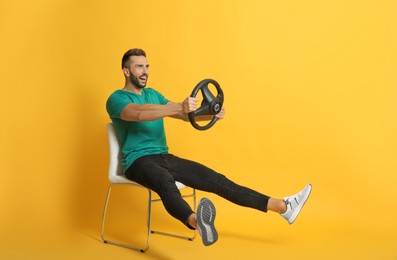 Photo of Happy man on chair with steering wheel against yellow background