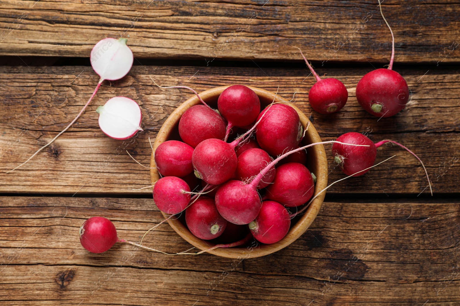 Photo of Bowl with fresh ripe radishes on wooden table, flat lay