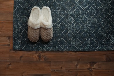 Photo of Stylish door mat and slippers on wooden floor, top view. Space for text