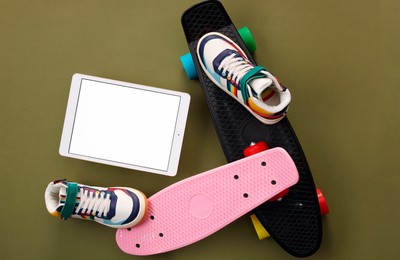 Photo of Modern tablet, skateboards and shoes on olive background, flat lay. Space for text