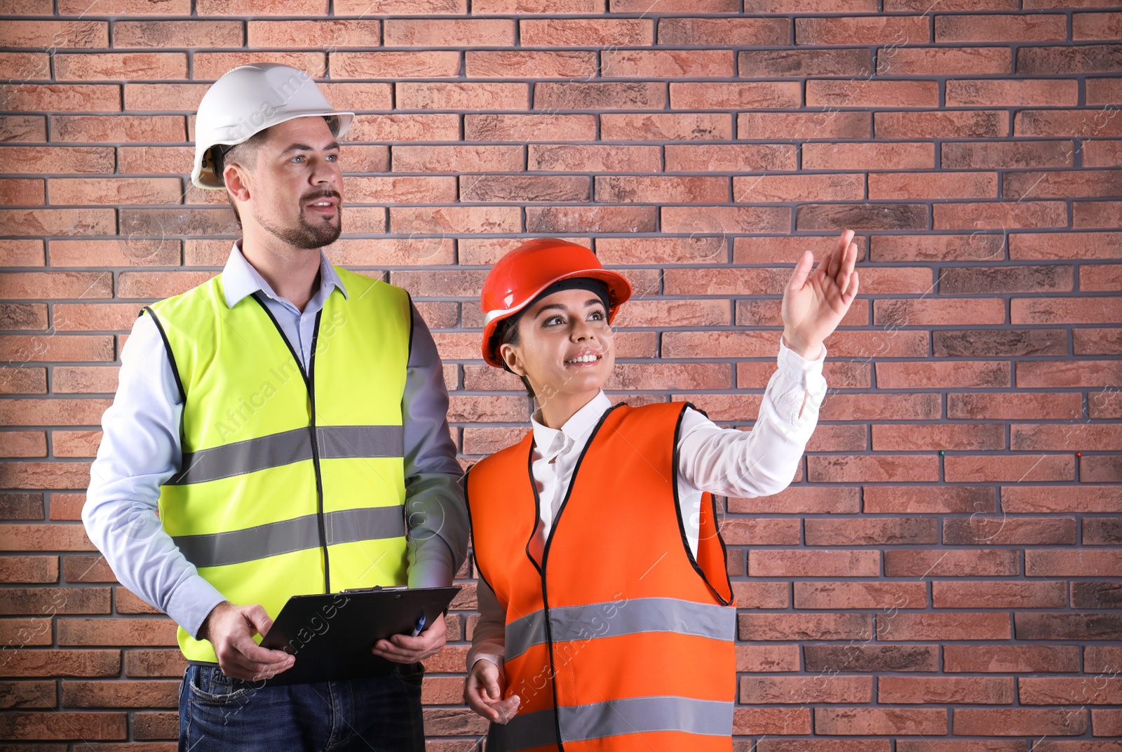 Photo of Industrial engineers in uniforms with clipboard on brick wall background. Safety equipment