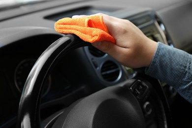 Photo of Man cleaning steering wheel with rag in car, closeup