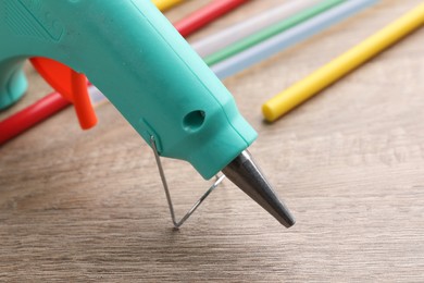 Photo of Turquoise glue gun and colorful sticks on wooden table, closeup