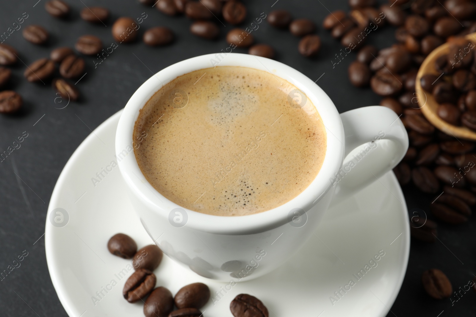 Photo of Cup of aromatic coffee and beans on grey table, closeup