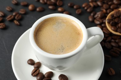 Photo of Cup of aromatic coffee and beans on grey table, closeup