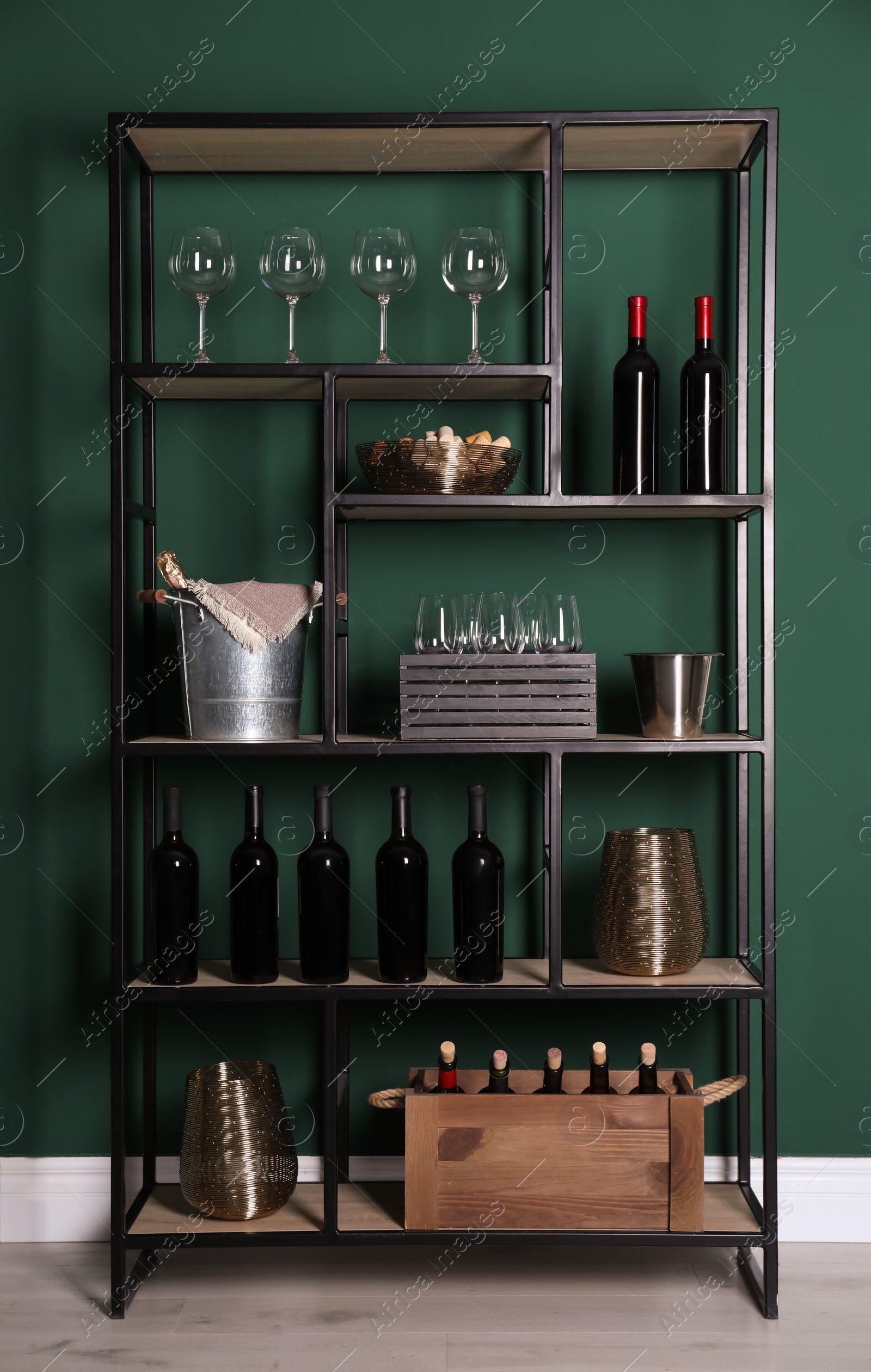 Photo of Rack with bottles of wine and glasses near green wall