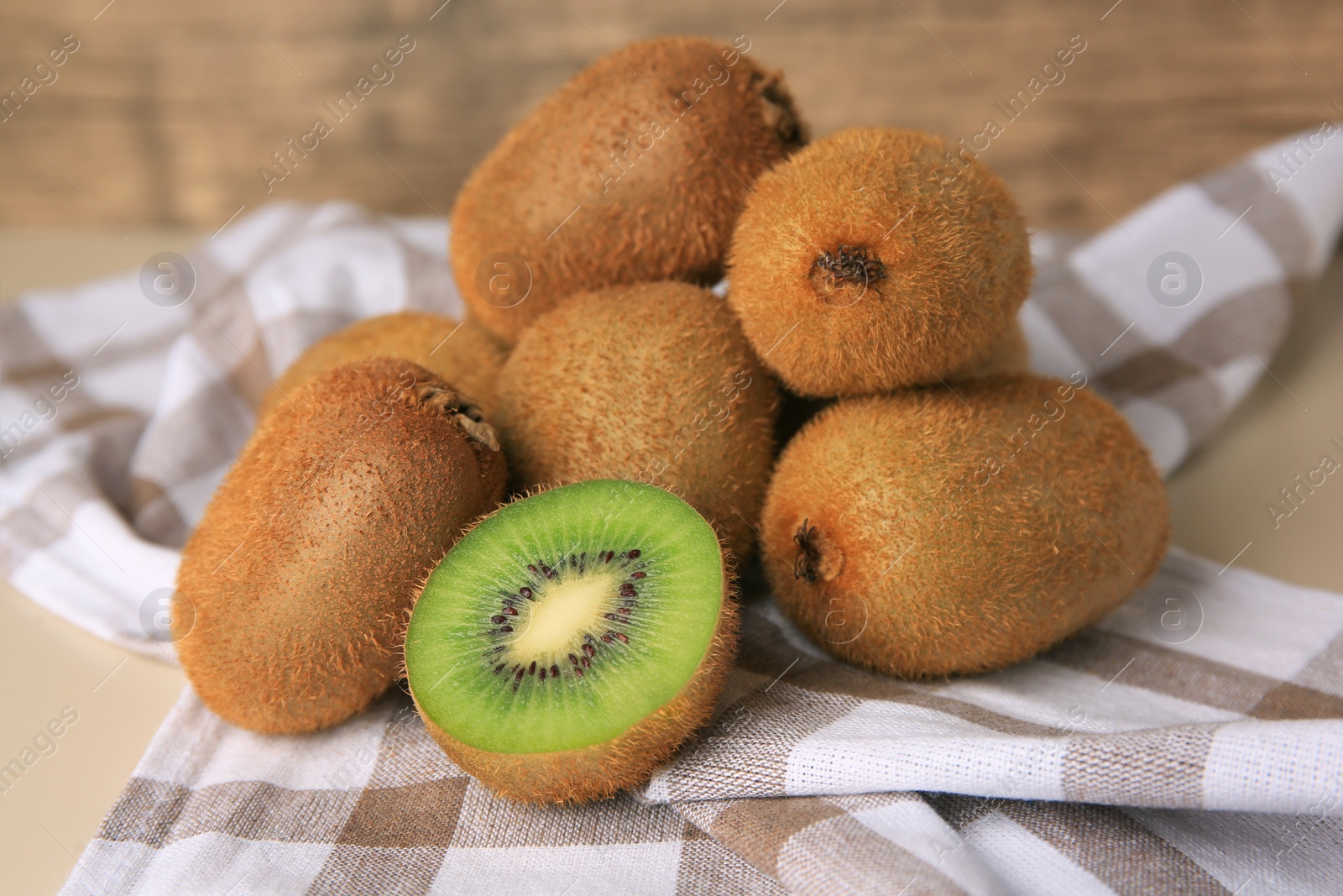 Photo of Heap of whole and cut fresh kiwis on beige table, closeup