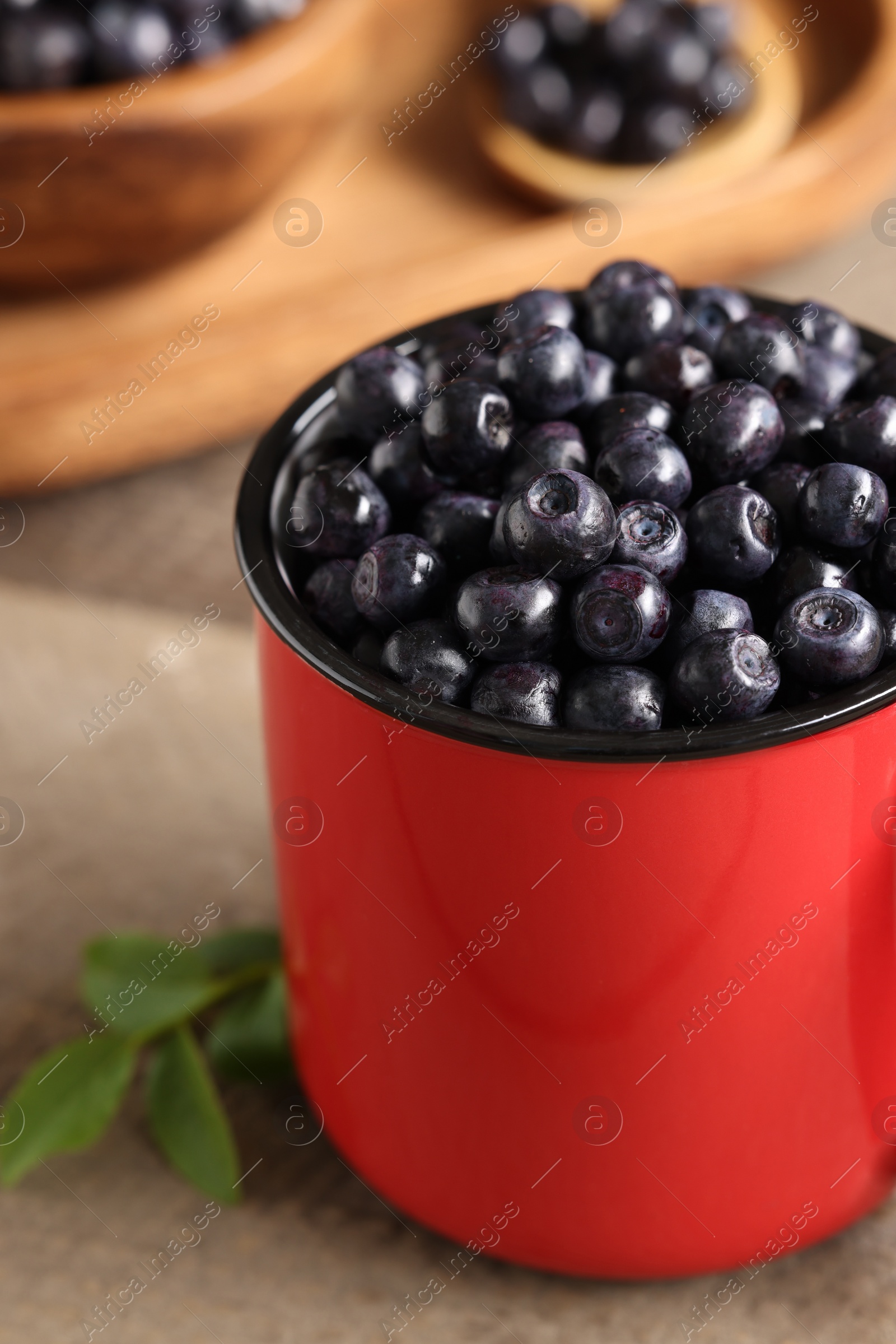 Photo of Red mug of tasty fresh bilberries on wooden table, closeup