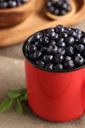 Red mug of tasty fresh bilberries on wooden table, closeup