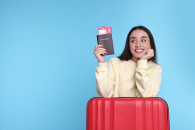 Photo of Smiling woman with passport, tickets and suitcase on light blue background. Space for text