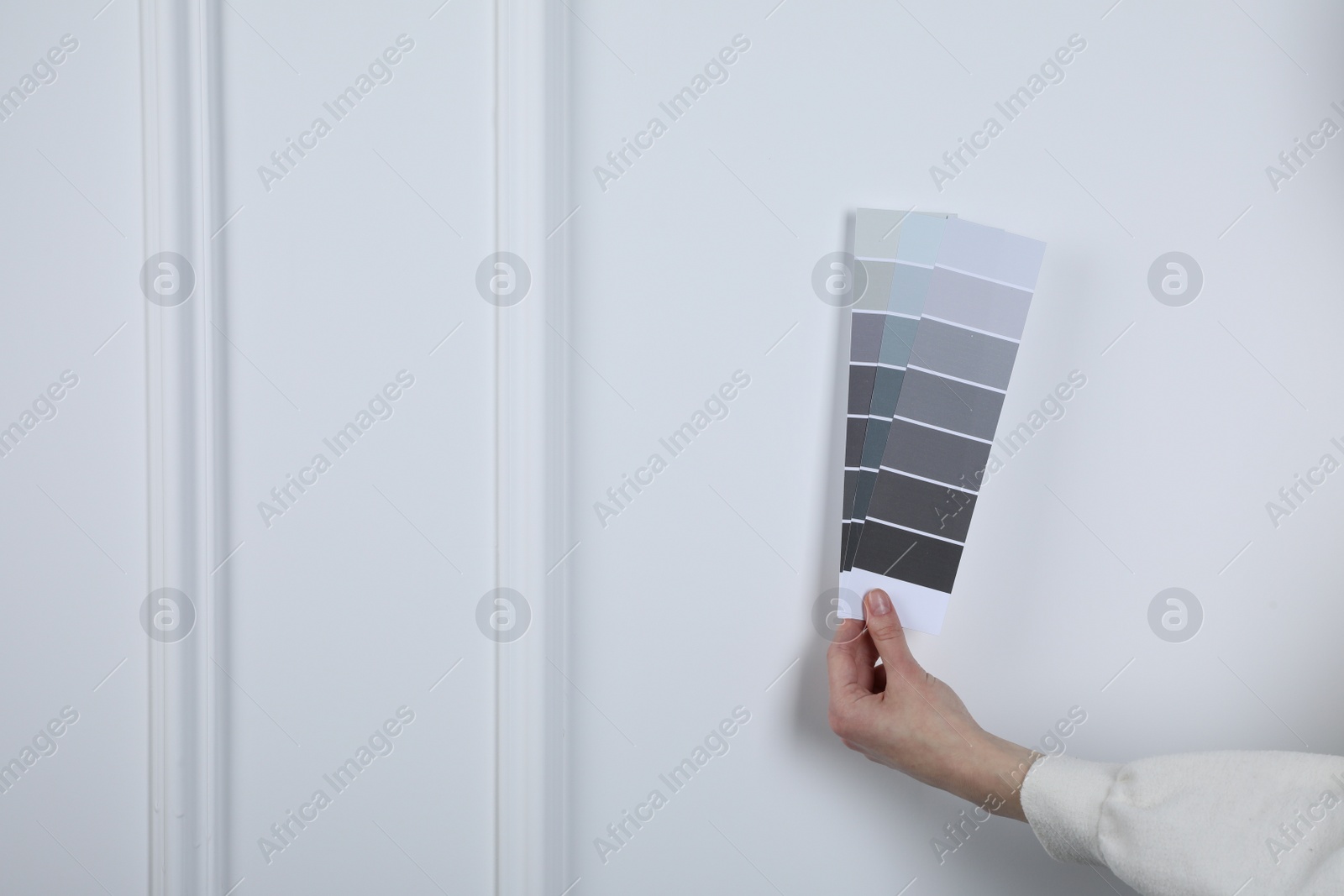 Photo of Woman with paint chips choosing color near white wall, closeup. Interior design