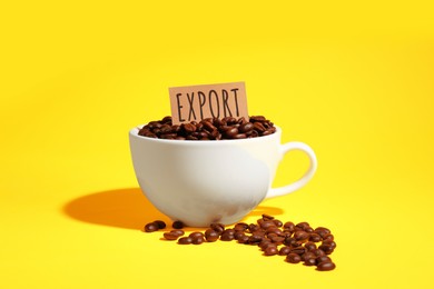 Photo of Coffee beans, white cup and card with word Export on yellow background