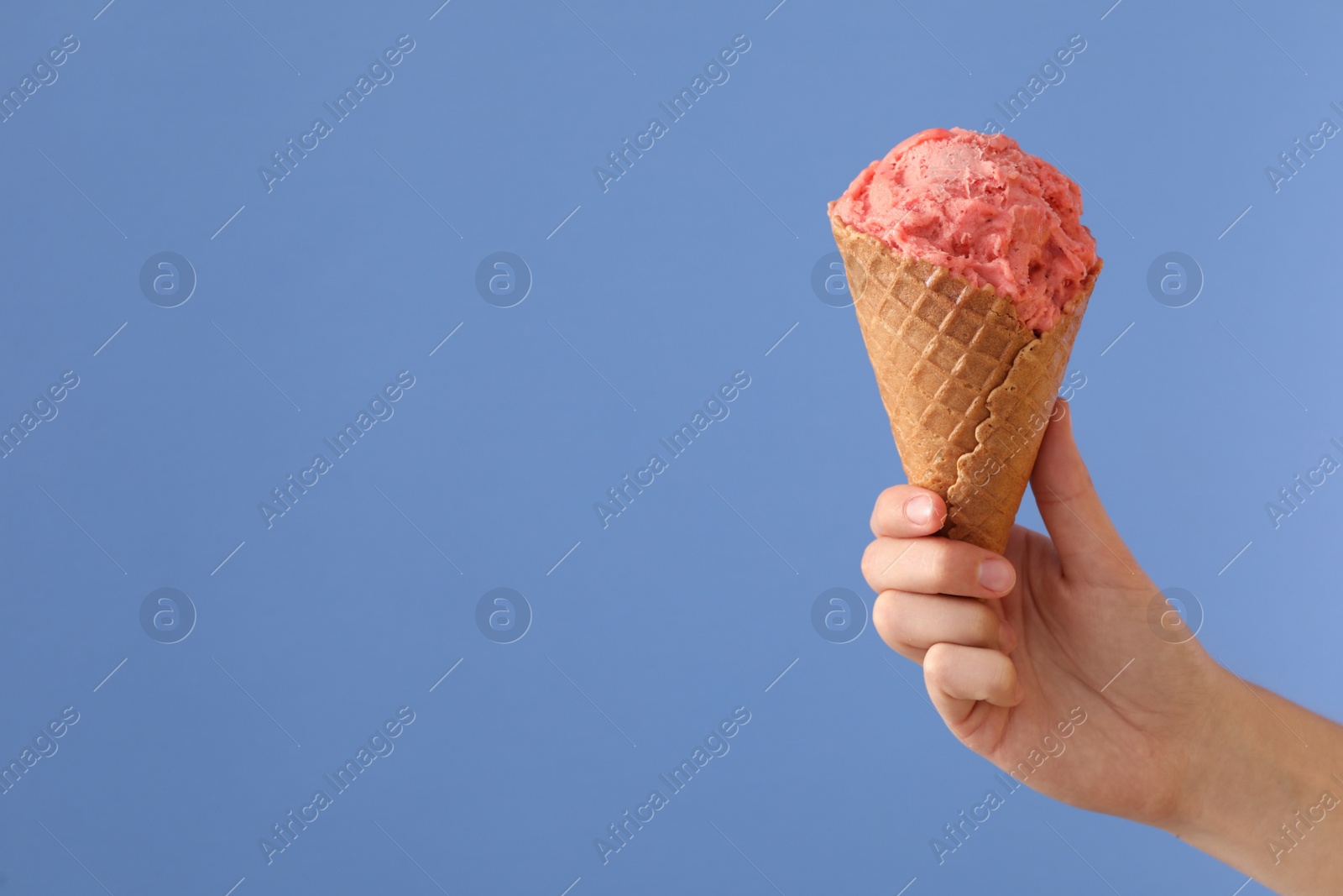 Photo of Woman holding pink ice cream in wafer cone on light blue background, closeup. Space for text