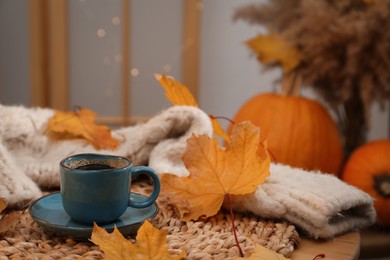 Photo of Cup of aromatic coffee, sweater and autumn leaves on table indoors, space for text