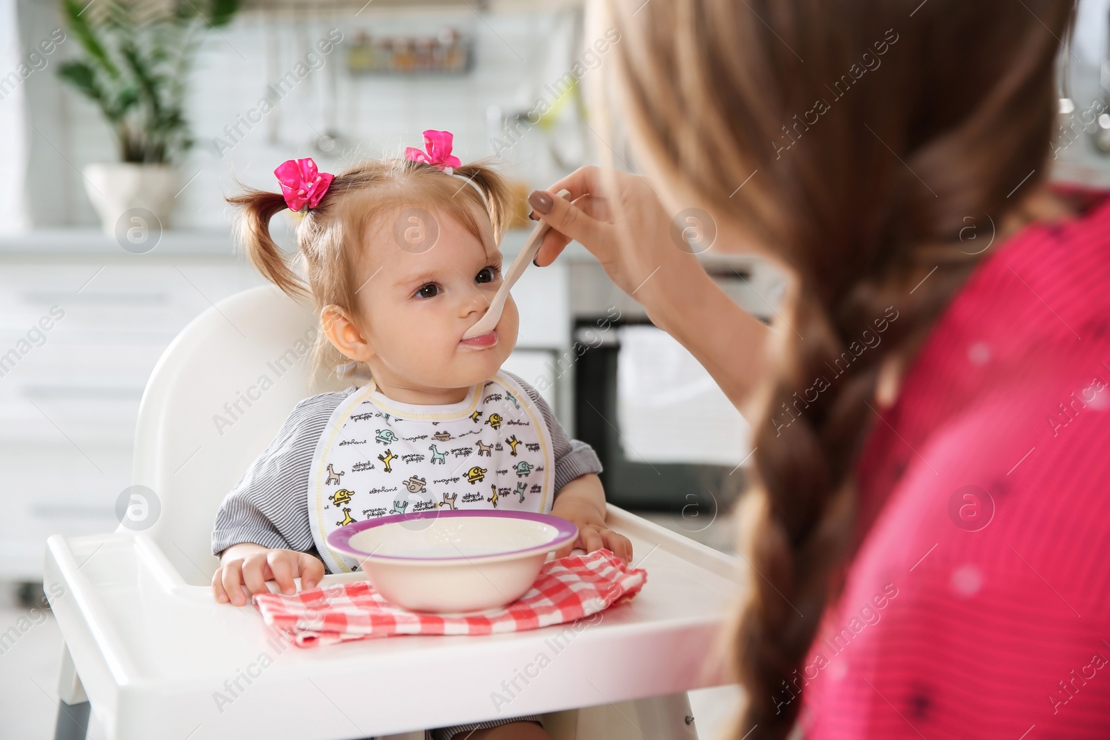 Photo of Mother feeding her little baby with healthy food in kitchen