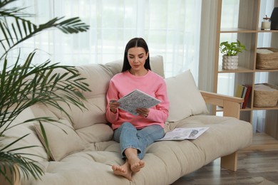 Young woman with antistress coloring page sitting on sofa in living room