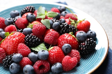 Photo of Many different fresh ripe berries in plate on grey table, closeup