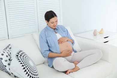 Beautiful pregnant woman sitting on sofa at home