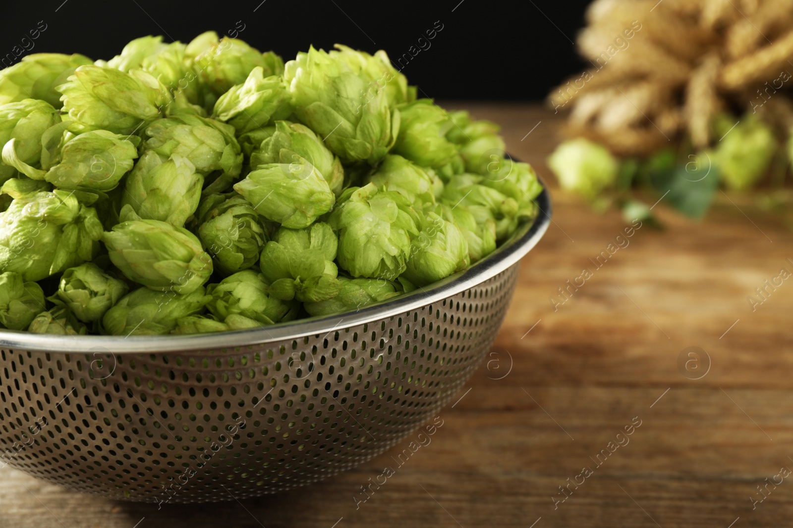 Photo of Fresh green hops in sieve on wooden table, closeup