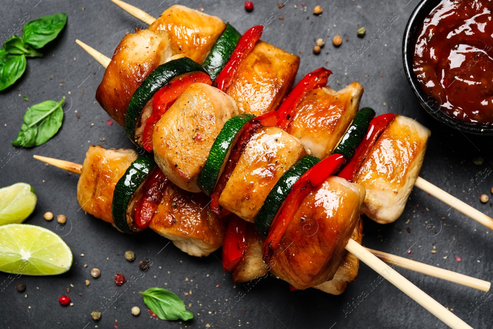 Photo of Delicious chicken shish kebabs with vegetables and sauce on black table, flat lay