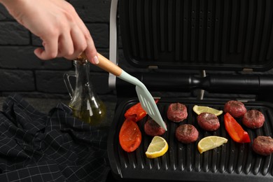 Photo of Woman cooking meat balls with bell pepper and lemon on electric grill at grey table, closeup