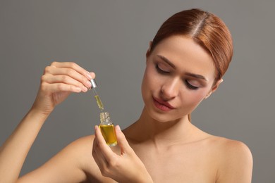 Photo of Beautiful young woman with bottle of cosmetic serum on grey background