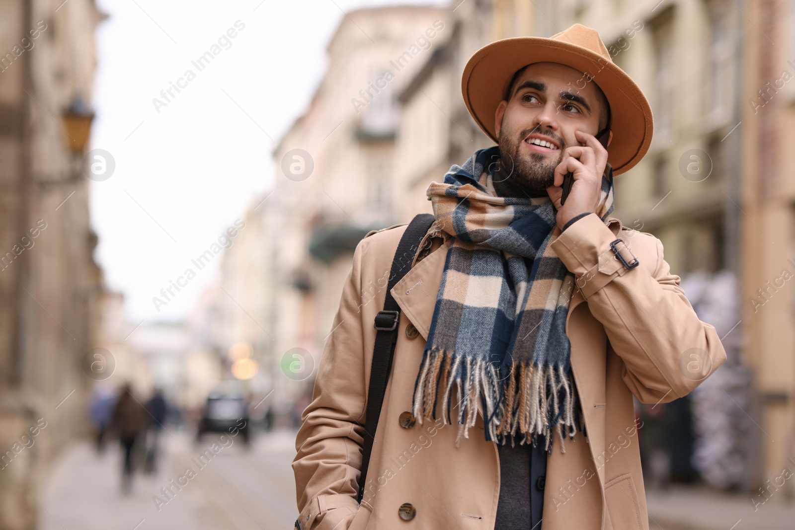 Photo of Smiling man in warm scarf with smartphone outdoors. Space for text