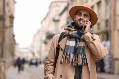 Smiling man in warm scarf with smartphone outdoors. Space for text