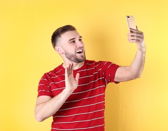 Young man using video chat on smartphone against color background