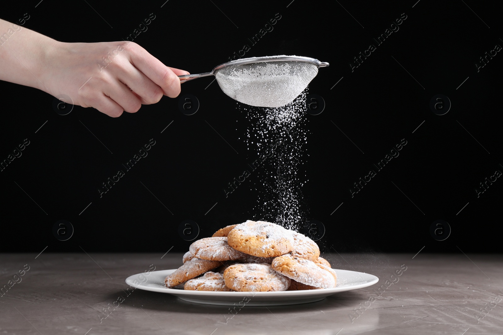 Photo of Woman with sieve sprinkling powdered sugar onto cookies at grey textured table, closeup