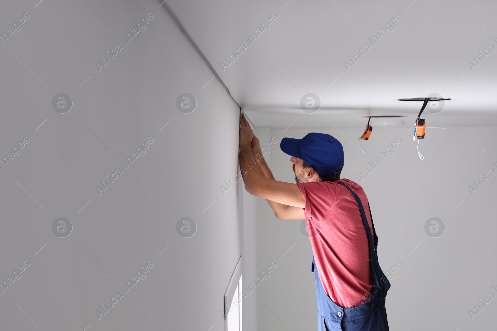 Photo of Worker installing stretch ceiling in empty room