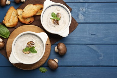 Photo of Delicious mushroom soup in ceramic pots and fresh ingredients on blue wooden table, flat lay. Space for text