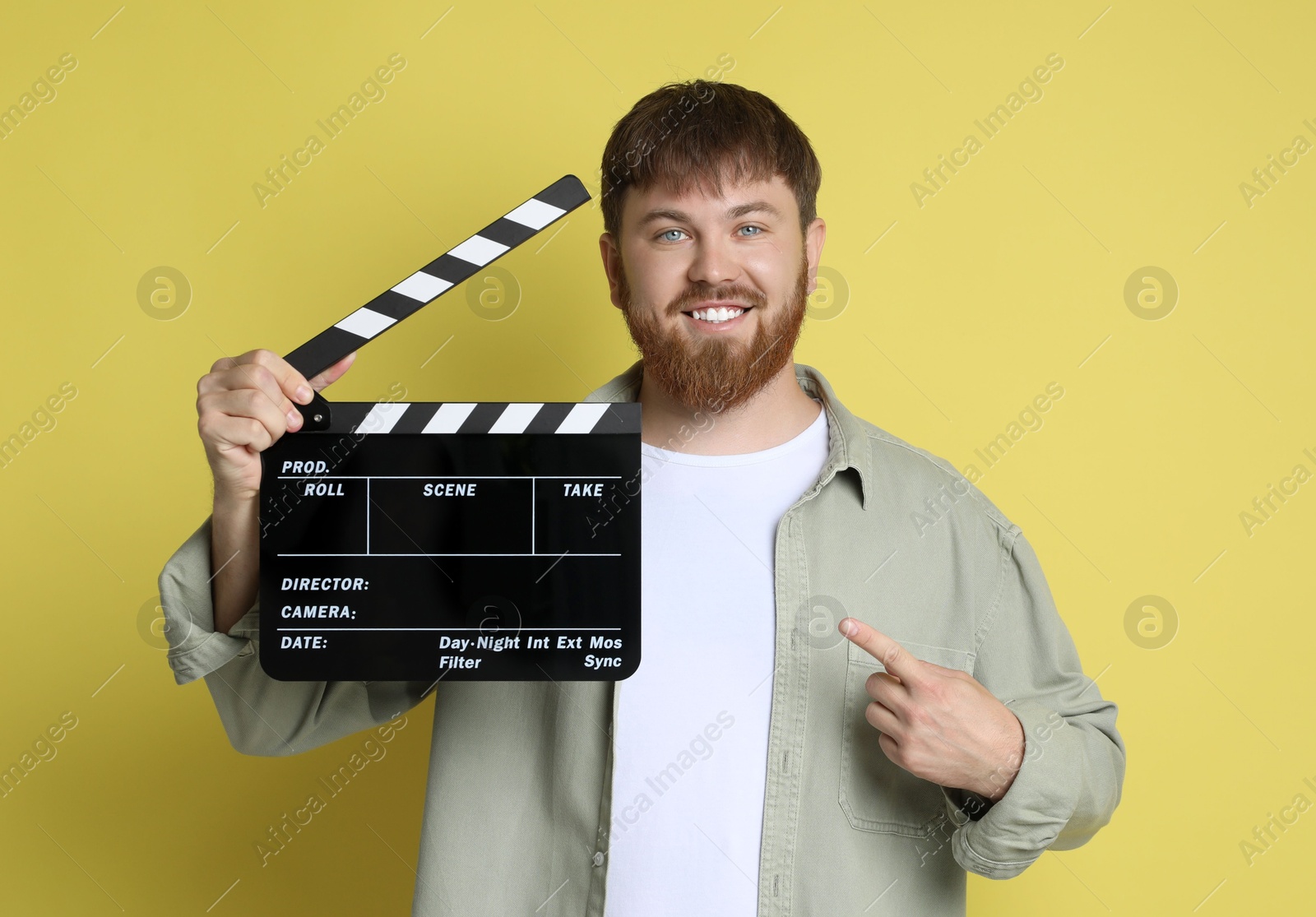 Photo of Making movie. Smiling man pointing at clapperboard on yellow background