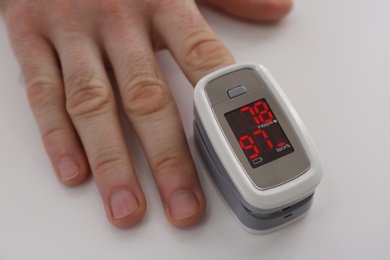 Photo of Man measuring oxygen level with modern fingertip pulse oximeter at white table, closeup