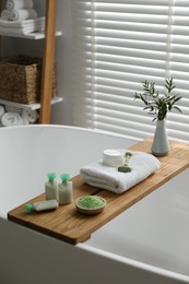 Wooden tray with spa products and green branches on bath tub in bathroom