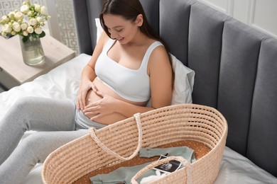 Beautiful pregnant woman making heart with hands on bed indoors