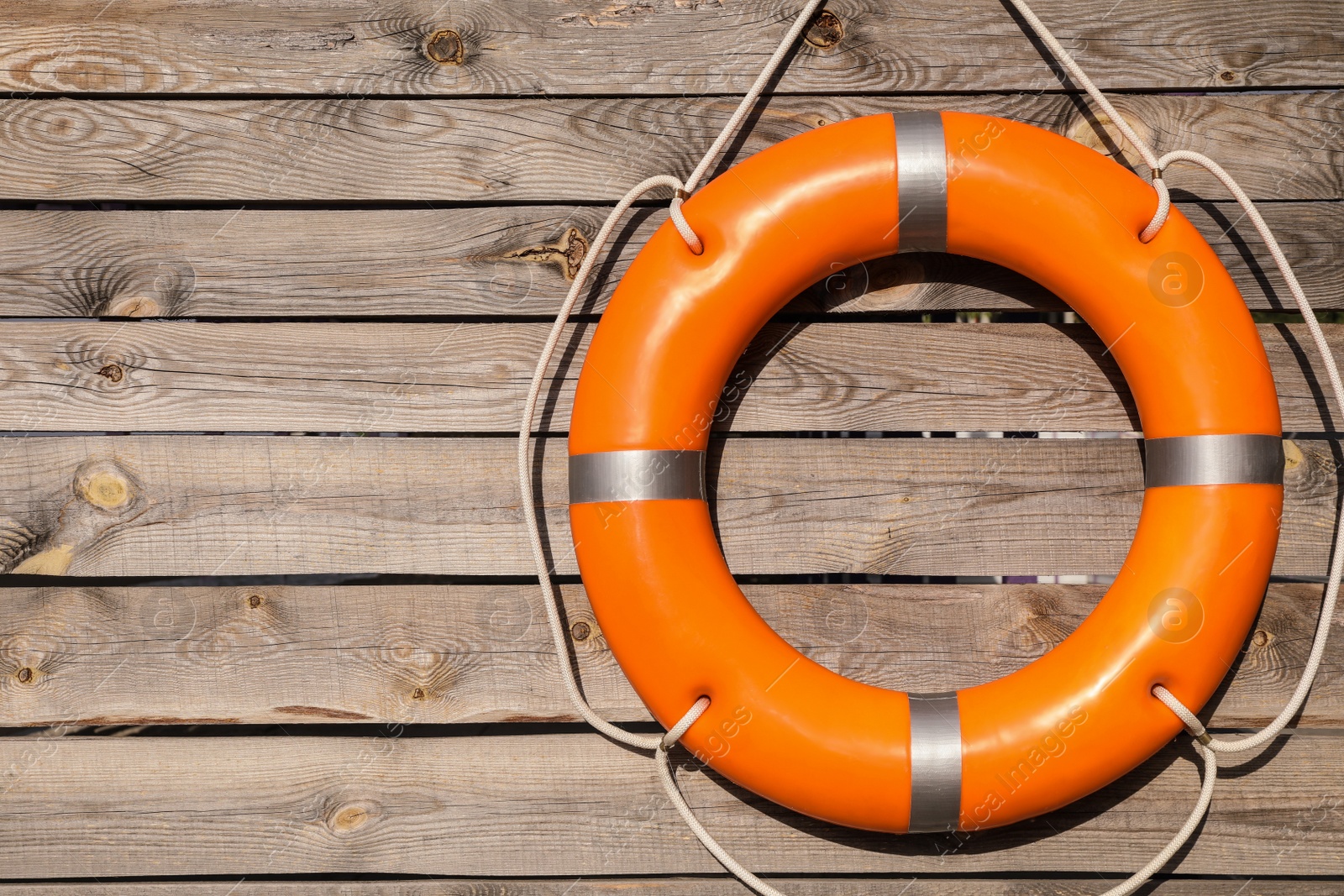 Photo of Orange life buoy hanging on wooden wall, space for text